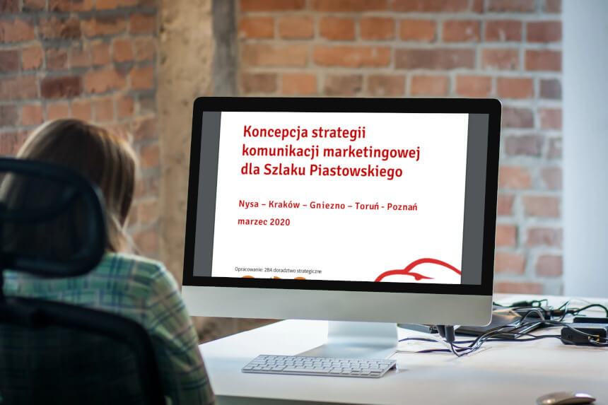 Kobieta siedząca przez monitorem komputera, czytająca "Koncepcję strategii komunikacji marketingowej dla Szlaku Piastowskiego"