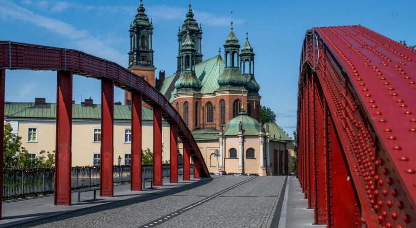 Po obu stronach zdjęcia czerwone przęsła mostu. Na wprost widok na poznańską katedrę.