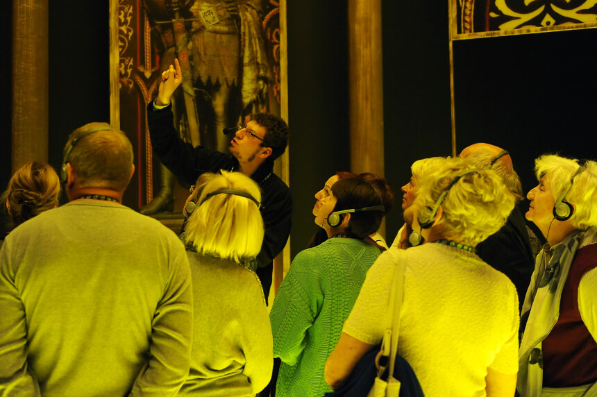 Grupa seniorów na ekspozycji Bramy Poznania. Patrzą w kierunku wskazanym przez przewodnika.