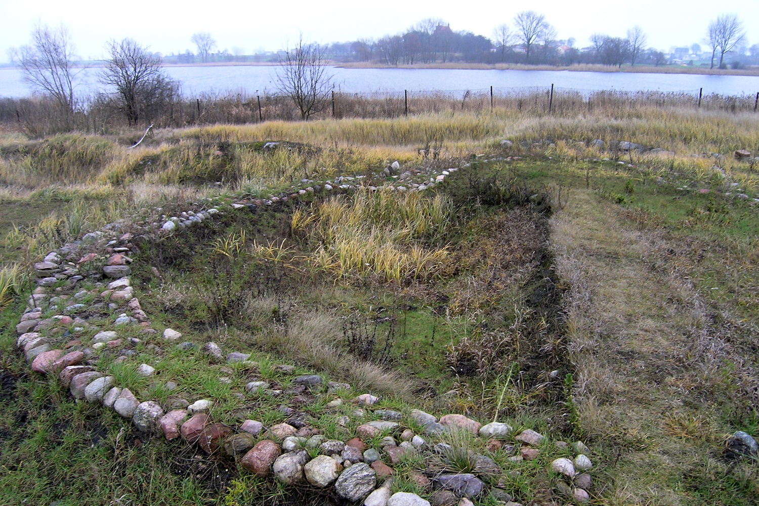 stanowisko archeologiczne - na brzegu jeziora pozostałości fundamentów zarośnięte niską roślinnością
